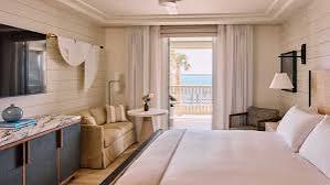 Coastal-style hotel guest room with a bed, wood-paneled wall, and ocean-view balcony